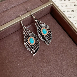 Detailed close-up of vintage silver leaf earrings with turquoise stones in a velvet box