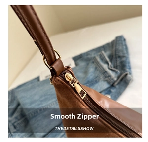 Close-up of smooth gold zipper and suede patchwork detail on a brown shoulder bag