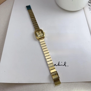 Detail view of a vintage rectangular gold watch with a brushed metal band on a magazine