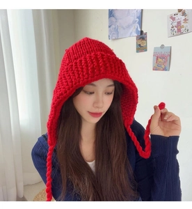 Détail d'un bonnet en grosse maille rouge avec des tresses et des protège-oreilles