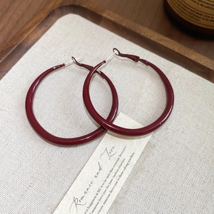 Detailed view of large dark red enamel hoop earrings on a textured beige display tray