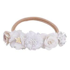 Detail of white lace and tulle flowers on a soft nude elastic headband for infants