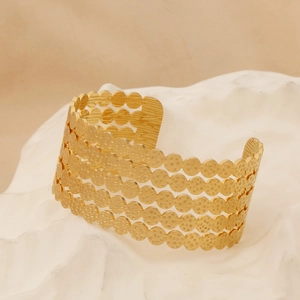 Detailed view of golden wide hollow hammered cuff bracelet on white stone base
