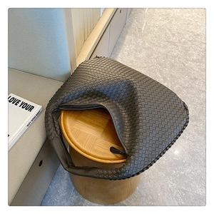 Detail shot of a dark grey woven leather handbag with zipper and fine texture on a wooden stool