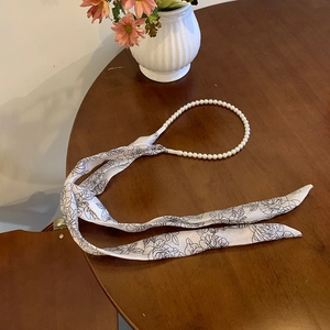 Close-up of pearl headband with elegant black rose printed silk ribbon on wooden desk
