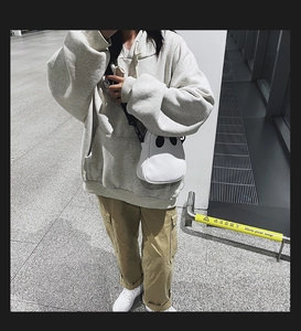 Street style shot of a white ghost-shaped crossbody bag paired with an oversized hoodie