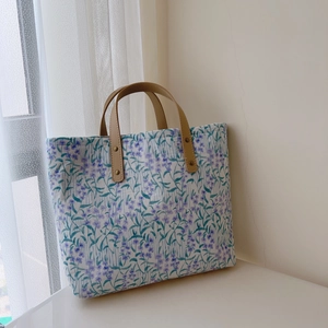 Détail d'un cabas en coton fleuri avec anses en cuir marron et rivets en métal