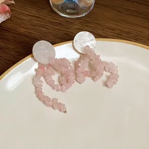 Pink natural stone tassel earrings with geometric silver needle studs on white ceramic plate