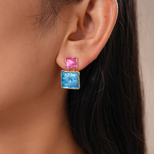 Close-up of square pink and blue enamel earrings with textured gold metal trim