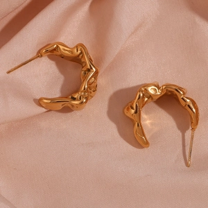 Detailed view of gold irregular wave earrings with a molten lava texture on pink silk