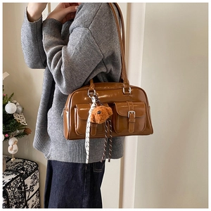 Detail of a brown glossy pillow bag with front buckle pockets and a plush bear charm