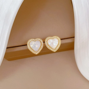 Detailed view of heart-shaped gold stud earrings with pavé crystals and pearl inlay