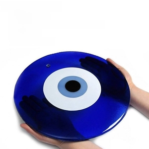 Close-up of a large blue glass evil eye wall decor held by hands to show size and scale