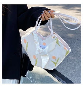Detail of white canvas tote featuring tulip embroidery and delicate ribbon handle decor