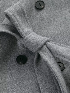 Close-up of grey wool coat showing double-breasted black buttons and tied waist belt detail