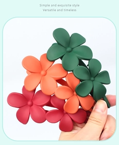 Close-up of matte floral hair clips in green, orange, and rose red held in hand