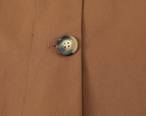 Close-up of brown twill coat fabric with a classic tortoise shell button and fine stitching
