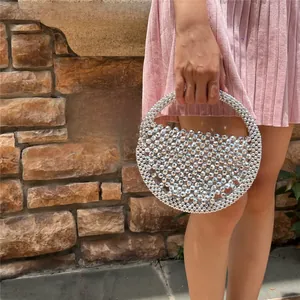 Close-up of handmade metallic beaded crescent handbag held by model against brick wall