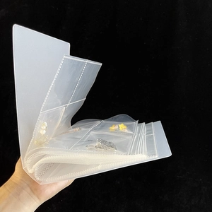 Detail showing hand holding transparent jewelry organizer book with multiple clear pockets