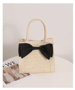 Detail of hand-woven straw bag with a large black bow ornament for beach fashion