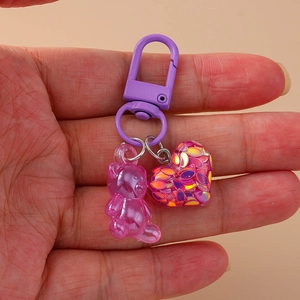 Cute resin bear and glitter heart keychain with purple clasp on a hand-held display