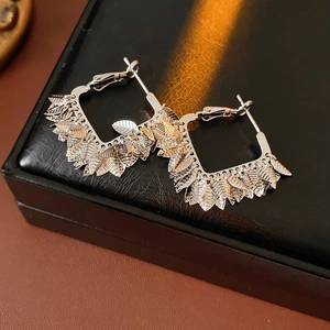 Macro detail of silver leaf square earrings on black leather surface showing fine texture