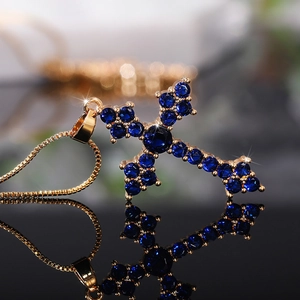 Macro detail of a golden cross pendant featuring deep blue crystal stones on black mirror