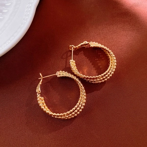 Detailed close-up of triple-layered golden twisted earrings on elegant dark satin fabric