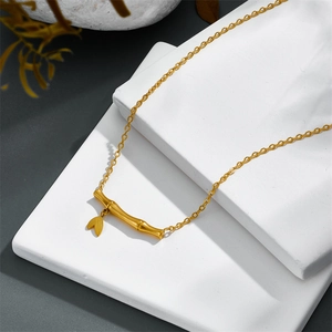 Golden titanium steel bamboo pendant necklace with leaf charm on white stone stand
