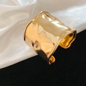 Macro detail of irregular gold cuff bracelet with high-shine metallic texture and ripples
