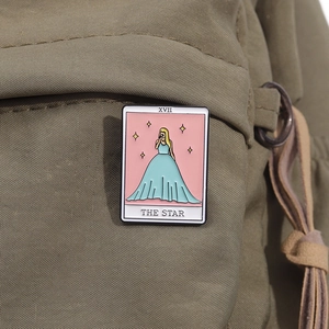 Macro detail of The Star tarot enamel pin featuring a singer on an olive green backpack