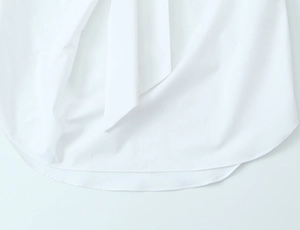 Close-up of the curved hemline and fine stitching on a white minimalist cotton shirt