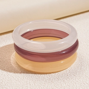 Close-up of three stacked resin bangles in transparent white, purple and yellow colors