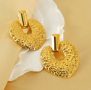 Détail de boucles d'oreilles en acier doré avec texture martelée et forme de coeur