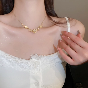 Close-up of a delicate gold flower and leaf pendant necklace worn on a woman's collarbone