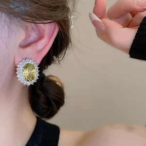 Macro shot of oval yellow gemstone earrings with white zircon accents on a model