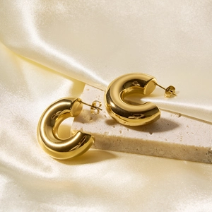 Close-up of gold hollow C-shaped earrings on elegant beige silk and stone texture