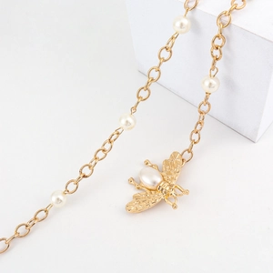 Golden chain belt with elegant pearls and a honey bee pendant on a white background