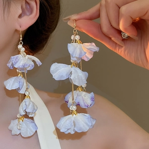 Détail de longues boucles d'oreilles fleurs en tissu violet avec perles et chaîne dorée