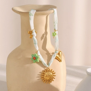 Collier bohème à ruban vert avec pendentifs soleil en or 18K et fleurs sur un vase en céramique