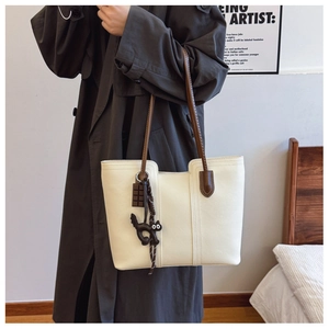 Detail of a creamy white leather tote bag with brown straps and cute cat charms on a model