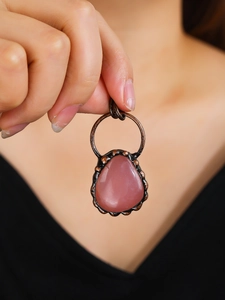 Retro bronze necklace with a teardrop pink gemstone pendant held in hand for display