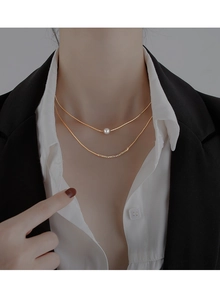 Close-up of double-layered gold necklace with baroque pearl and textured metal bar