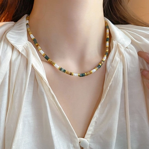 Detail of ethnic beaded necklace with white, green and gold beads on a silk shirt