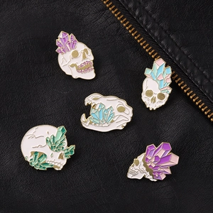 Detailed set of five skull enamel pins with colorful crystals on black leather background