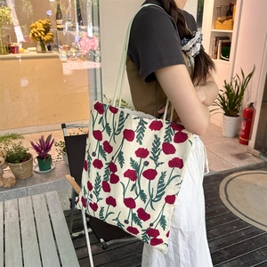 Détail d'un cabas en toile à fleurs rouges porté par un mannequin dans un cadre décontracté
