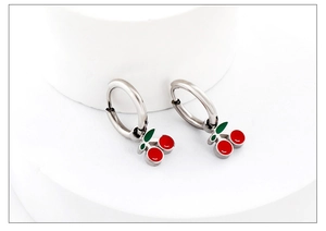 Detail of silver hoop earrings featuring cute red and green cherry pendants on a stand