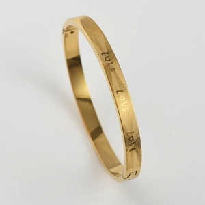 Detail view of gold titanium steel bangle with Love engraving and secure buckle clasp