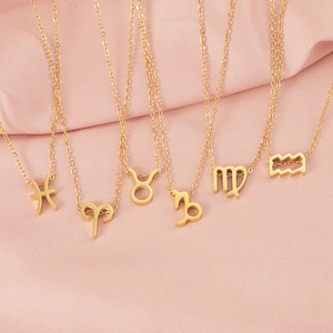 Gold zodiac sign necklaces collection featuring diverse astrological symbols on pink cloth