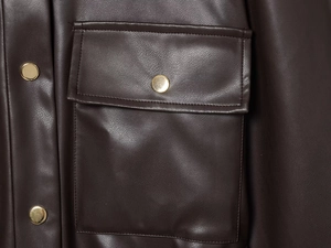 Détails rapprochés d'une veste en similicuir marron foncé avec bouton doré et coutures
